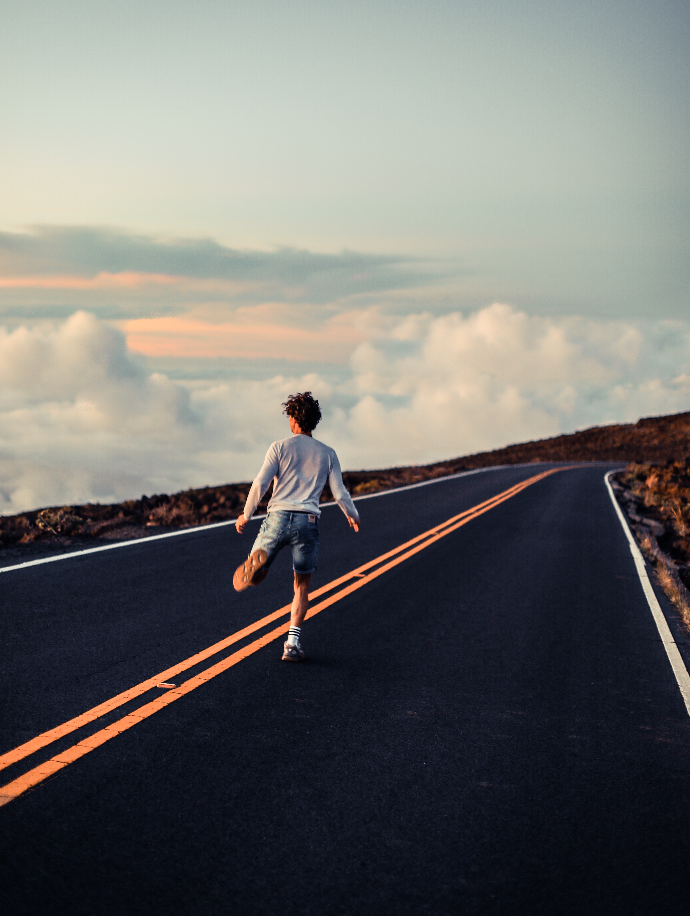 Un ragazzo corre sulla strada che conduce alla cima del vulcano Haleakala sull'isola di Maui, Hawaii. è come se corresse sopra ad un mare di nuvole.
